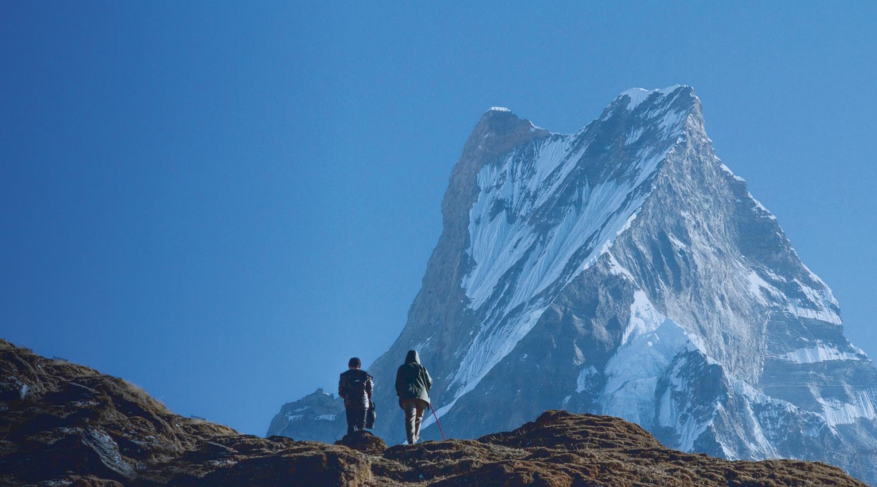 Two people walking on a mountain in Hindu Kush Himalaya. View with a peak behind and a blue sky.