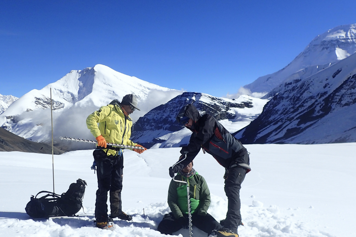 three people installing mass balance stakes in a snowy mountain environment