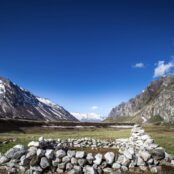 blue sky with grey mountains, green grass and a circle of rocks
